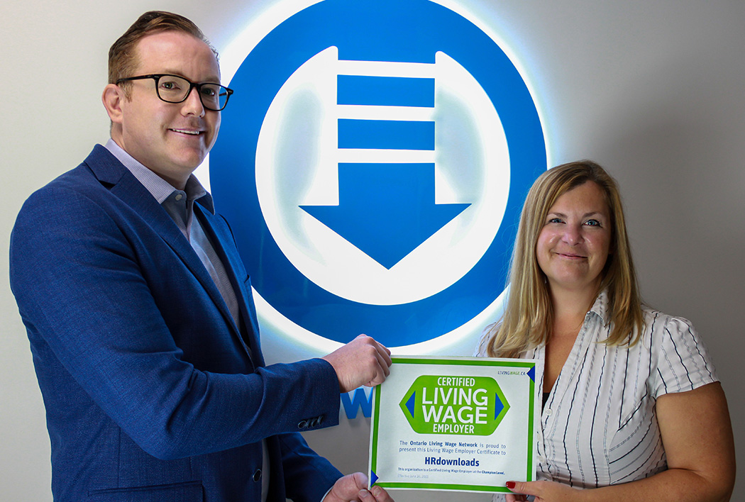 Neil Poutney and Sharon Bunce standing in front of HRdownloads logo, holding the Living Wage Certified Certificate