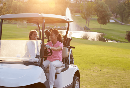 Two women in a golf cart on a golf course smiling