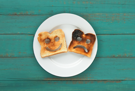 Two pieces of toast on a plate. One has a happy face and one has a sad face