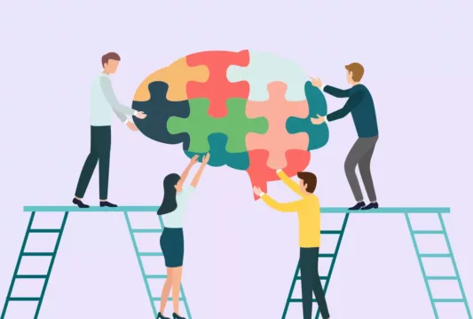 Employees on ladders putting puzzle pieces together to make an image of a brain