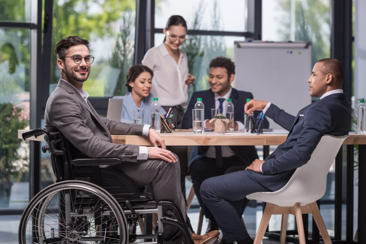 employees in a meeting around the table sitting on chairs except for one sitting in a wheelchair