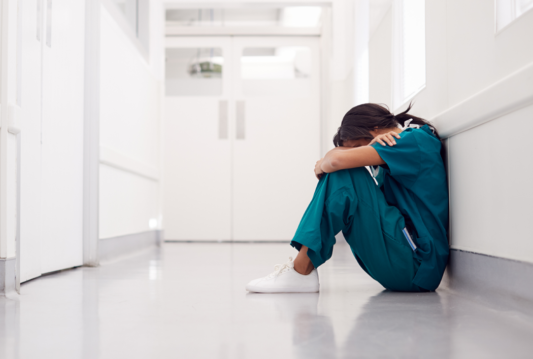 Healthcare worker sitting in the hallway of a hospital on the floor
