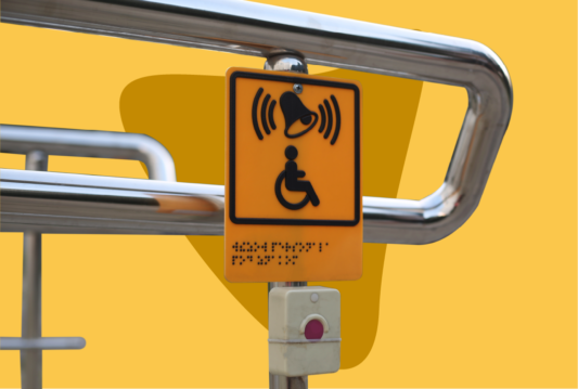 A yellow accessibility sign posted above a red button.