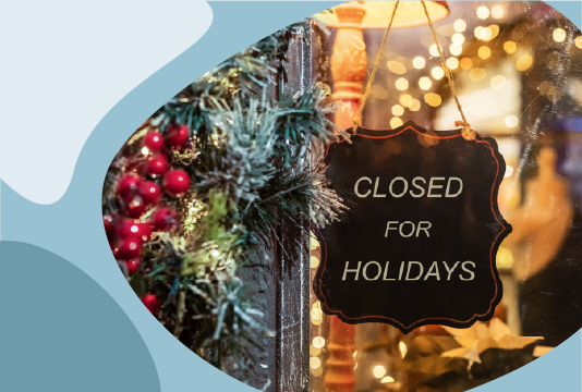 A sign is hanging on a door to a storefront that reads, "closed for the holidays." The storefront is decorated in a winter holiday theme.