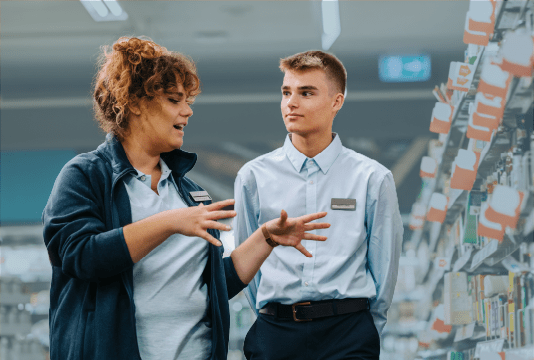 Performance Improvement Plan: A senior employee is standing beside a junior employee in a grocery store and is explaining something to them.