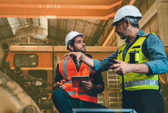 Health and Safety Training Programs: A trainer and trainee are talking while wearing PPE in an industrial workplace